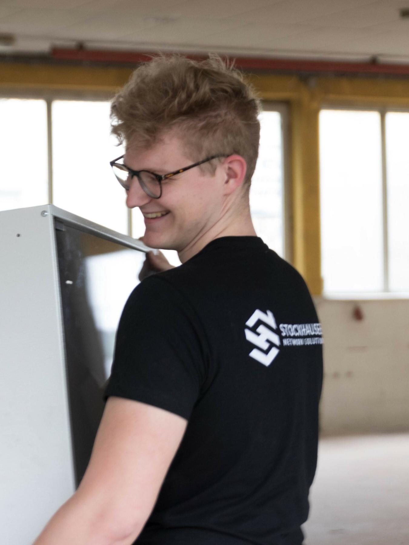 Max Stockhausen lacht bei der Arbeit an einem Netzwerkschrank